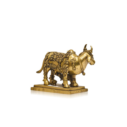 A small decorative brass-colored cow figurine with ornate engraved details, standing on a rectangular base